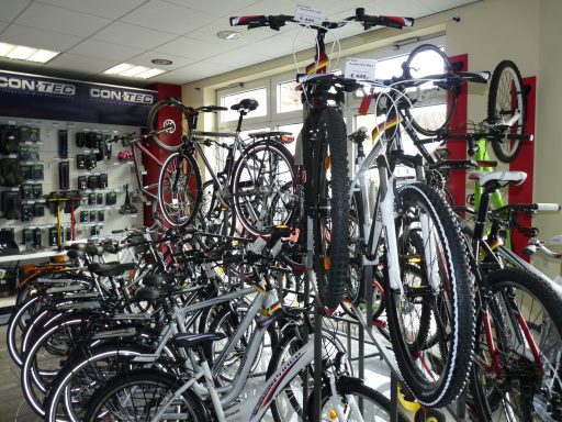 Ein schwarzes und ein weißes Mountain-Bike befinden sich auf einem Päsentationsständer. Rings rum befinden sich noch viele andere Fahrräder.