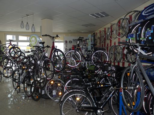 Zahlreiche Fahrräder sind im Verkaufsraum arrangiert. Im Hintergund befindet sich die Eingangtür. 