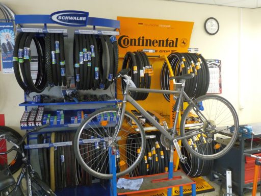 Auf einem Montagebock steht ein Kundenfahrrad zur Reparatur vor einer blauen Markenwand von Schwalbe und einer geleben von Continental.