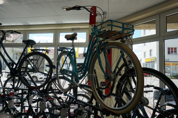 Ein blaues Hollandrad. Das Fahrrad hat einen vorderen blauen Gepäckträger mit Holzboden. Die Reifen sind beige. 