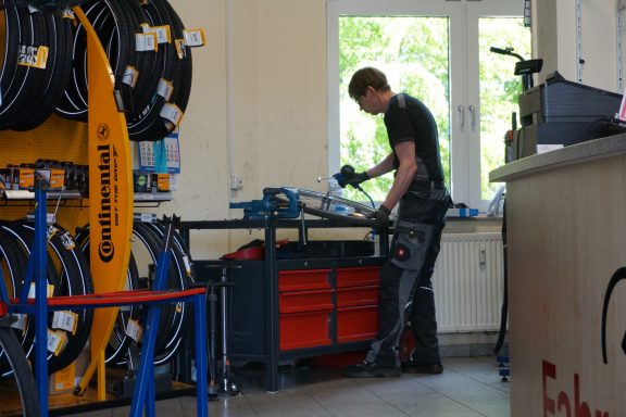 Stefan Stark, der Ladeninhaber bei einer Reparatur. Er hält einen Kompressorschlauch in der Hand zum Luftpumpen. 